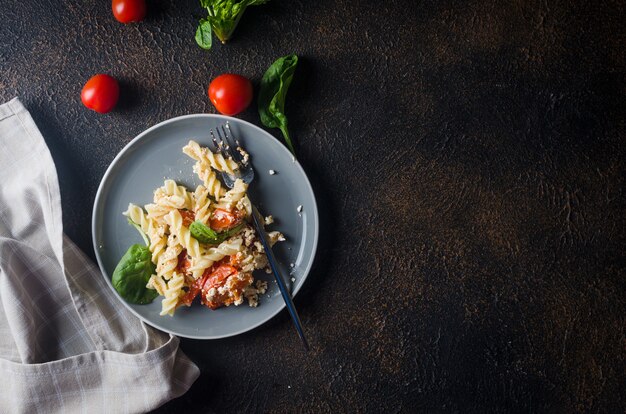 暗い背景に焼きたてのフェタチーズとトマトを混ぜたパスタのイタリア料理。フェタパスタ。トレンドのバイラルレシピ、フラットレイ、コピースペース