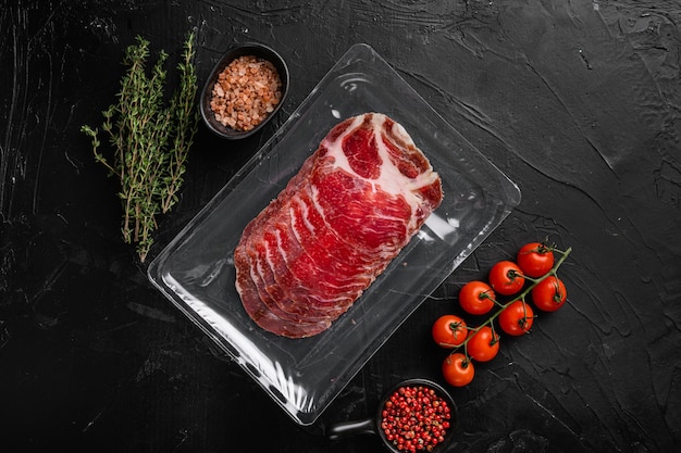 Italian dry cured ham vacuum pack set, on black dark stone table background, top view flat lay, with copy space for text