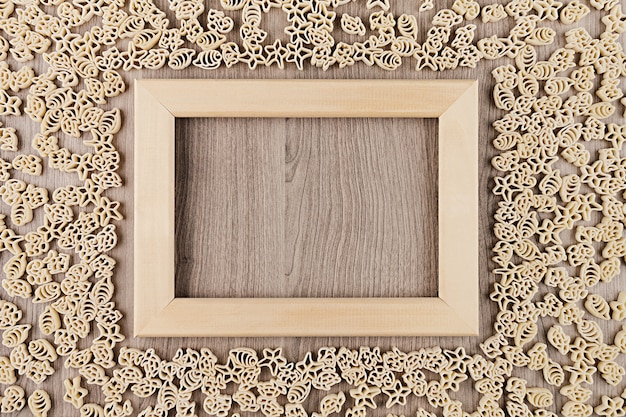 Photo italian dry sea pasta on beige brown wooden board with empty copyspace as decorative frame background