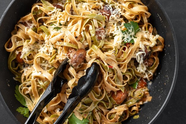 Italian fettuccini pasta closeup Black pasta tongs with pasta Pasta alfredo with mushrooms