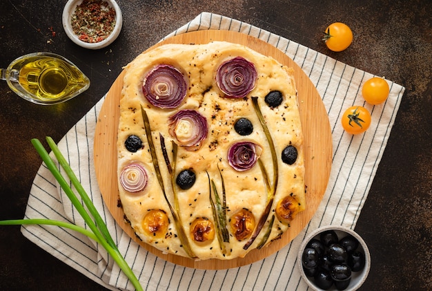 italian focaccia bread with vegetables and herbs on dark table with ingredients flower art focaccia