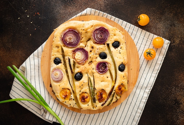 Italian focaccia bread with vegetables and herbs on striped tablecloth Garden focaccia