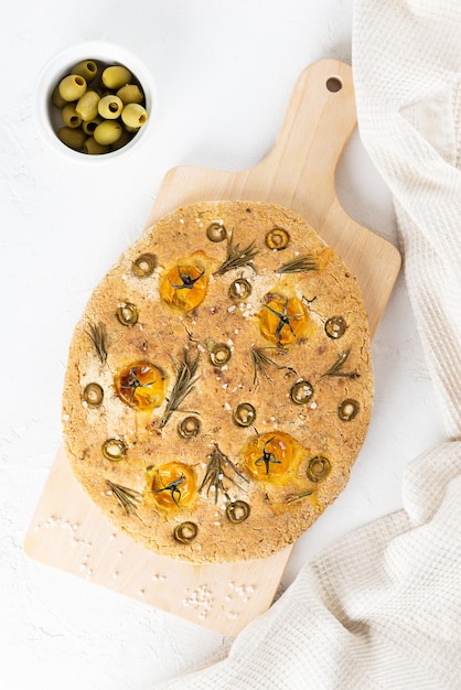 Italian focaccia with olives tomatoes rosemary and spices with a linen towel on the table