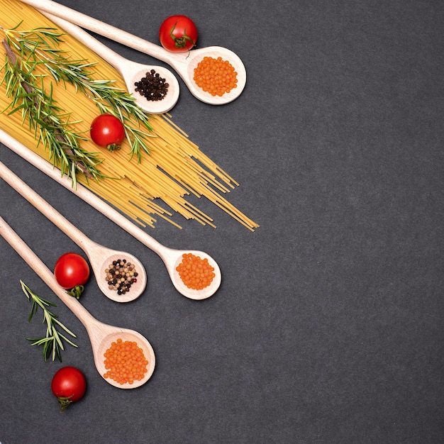 Italian food ingredients.Still life of cooking pasta on a black background top view. Wooden spoons with spices. Frame of products and vegetables.