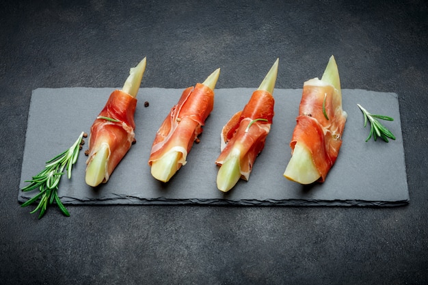 Italian food with melon and prosciutto on stone board