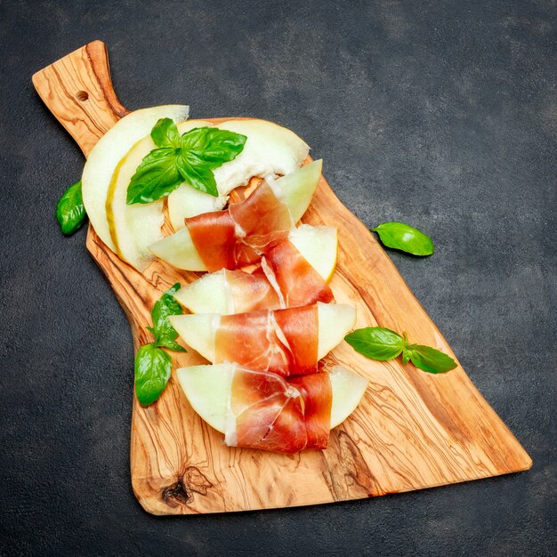 Italian food with melon and prosciutto on wooden cutting board