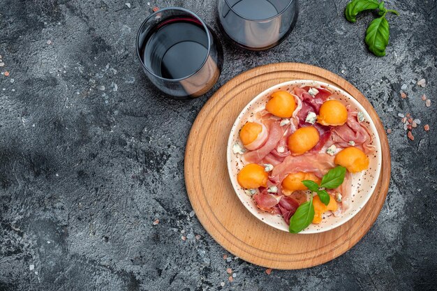 Italian food with red wine melon and prosciutto cantaloupe\
melon with prosciutto or jamon and green basil leaves with glass of\
wine restaurant menu antipasti appetizer cookbook recipe top\
view