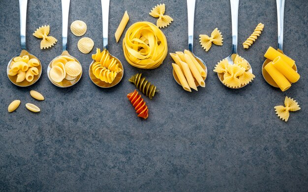 Italian foods concept and menu design. Various kind of pasta on dark stone background with flat lay.