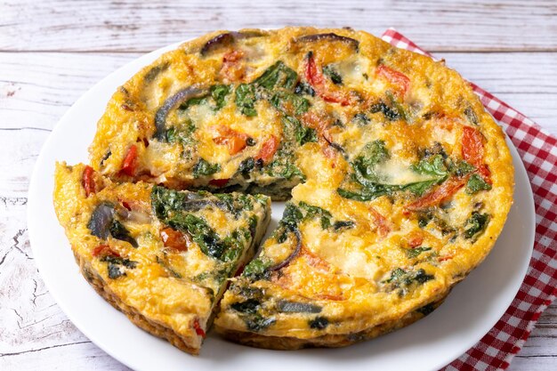 Italian Frittata made with spinach tomatoes onion and peppers on white wooden table