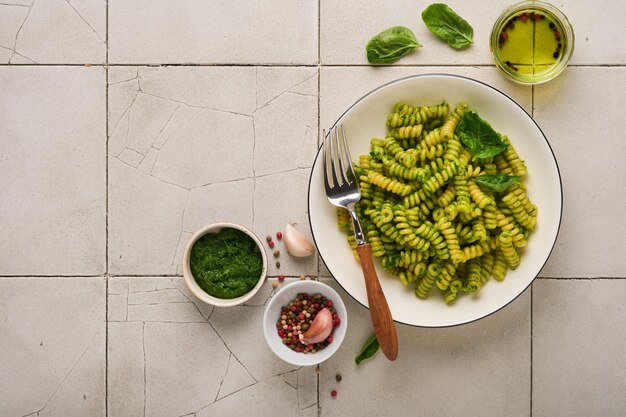 写真 イタリアのフジッリパスタとペストフジッリパスタとバジルペストとハーブパルメザンチーズバジルとニンニクの白いプレートに古いひびの入ったタイルテーブルコンクリートの背景上面図モックアップ