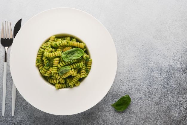 Italian Fusilli Pasta with Pesto Fusilli pasta with basil pesto and herbs parmesan cheese basil and garlic on white plate on grey stone countertop background Top view Copy space Mock up