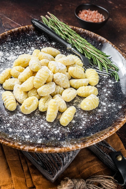 Foto gnocchi di gnocchi italiani gnocchi di patate crude su piastra con timo sfondo scuro vista dall'alto