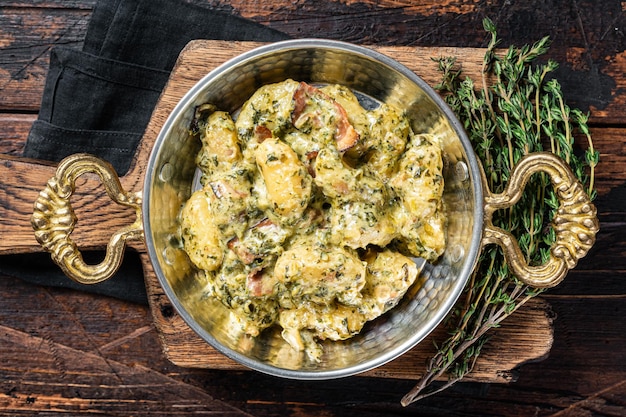 Italian Gnocchi potato pasta with spinach and parmesan in skillet Wooden background Top view