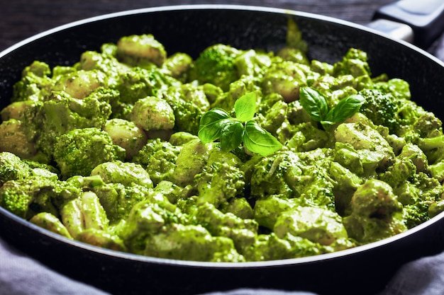 Italian gnocchi with broccoli florets tossed with basil pesto and creamy cheese sauce in a skillet, close-up, landscape view from above