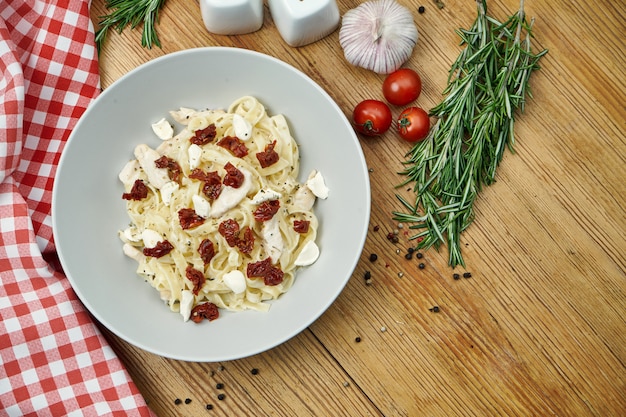Italian homemade tagliatelle with dried tomatoes, chicken and mozzarella in a beige pial on wood.