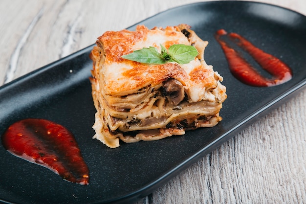 italian lasagna with tomato sauce on a black plate and wood background top view