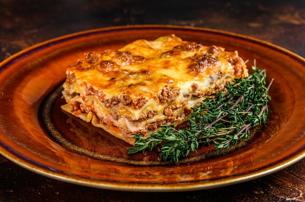 Foto lasagne italiane con salsa bolognese di pomodoro e carne di manzo tritata su un piatto rustico. sfondo scuro. vista dall'alto.