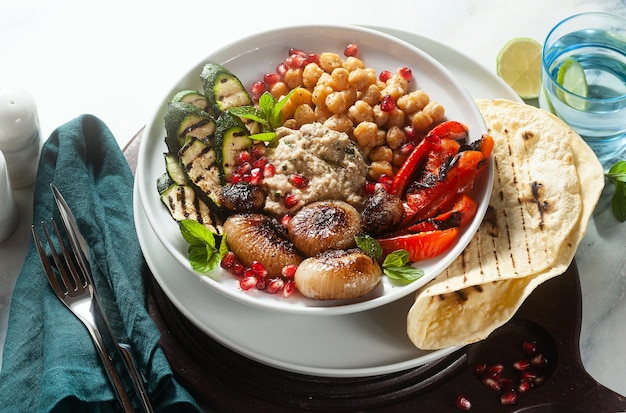 Ciotola del buddha del mediterraneo italiano con baba ghanoush cipolle caramellate ceci piccanti e verdure grigliate cibo vegano sano e pane pita