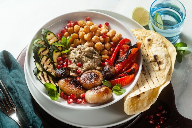 Ciotola del buddha del mediterraneo italiano con baba ghanoush cipolle caramellate ceci piccanti e verdure grigliate cibo vegano sano e pane pita