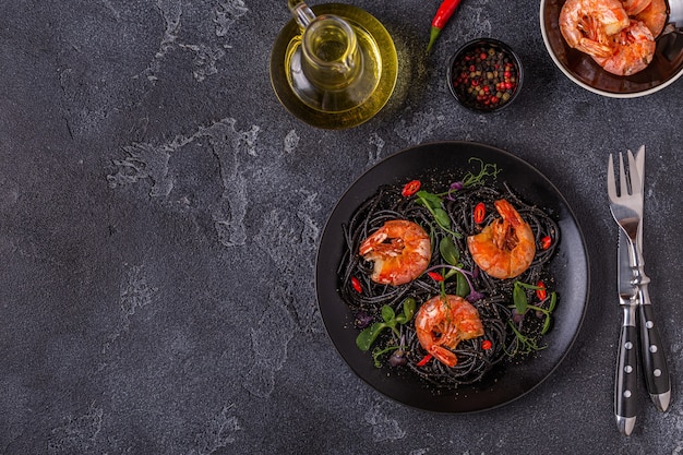 Italian pasta black spaghetti with shrimp and microgreens, top view.