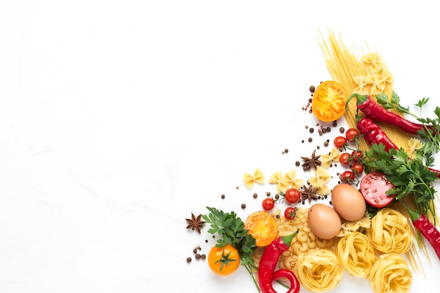 Italian pasta of different kinds with spices, red hot pepper, chicken eggs, yellow and red tomatoes on a white stone background. Concept cooking Italian pasta and sauce. Flat lay, top view