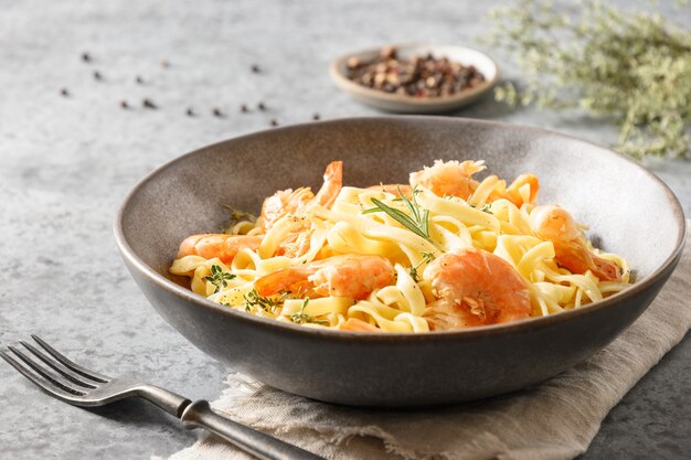 Italian pasta fettuccine with shrimps decorated rosemary sprig in bowl on gray table. Close up.