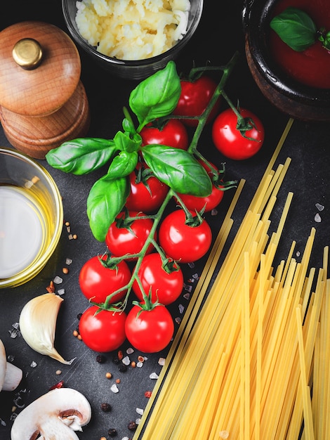 Ingredienti per la pasta italiana. pomodorini, pasta spaghetti, aglio, funghi, basilico, olio d'oliva, mozzarella e spezie su sfondo scuro grunge