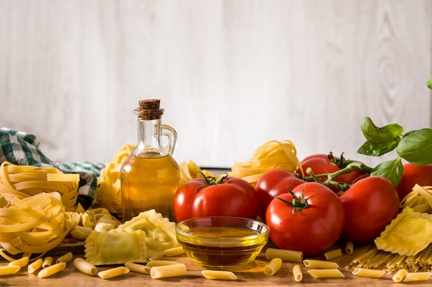 イタリアのパスタと食材のラビオリ、ペンネパスタ、スパゲッティ、トルテリーニ、トマト、バジルの木製テーブル