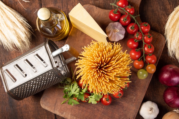 Photo italian pasta (macaroni),  tomatoes, olive oil, cheese and spices on rustic wood, top view.