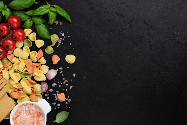 Italian Pasta orecchiette with traditional ingredients for the preparation food on black table. Culinary food cooking background. Top view.