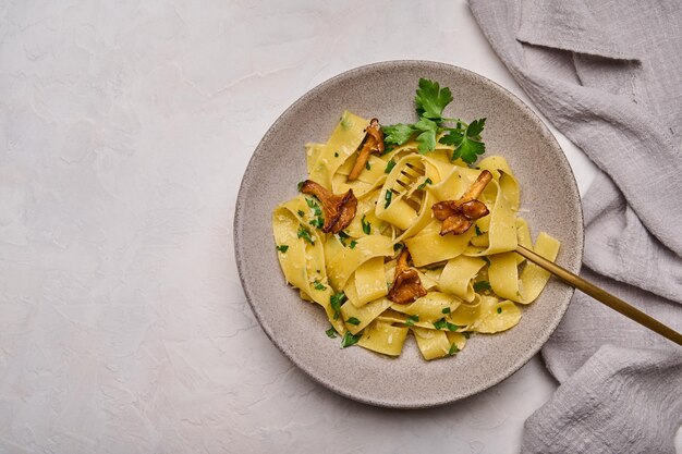 イタリアのパスタパッパルデッレとキノコのアンズタケチーズとパセリのプレートに金色のフォーク