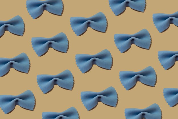 Italian pasta pattern on a yellow backdrop. blue color of bow\
tie farfalle pasta viewed from above. top view. repetition seamless\
pattern. food background.