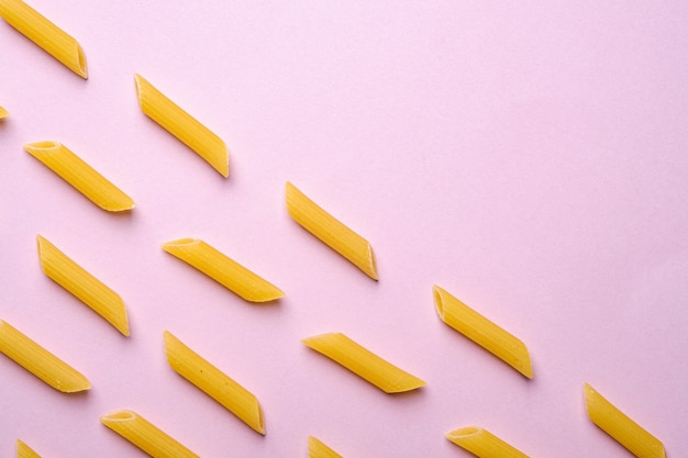 Italian pasta, raw penne tube macaroni on pink table, top view copy space, abstract food