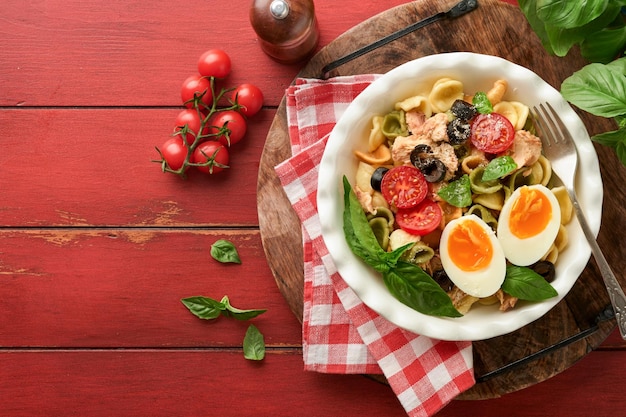 Italian pasta salad Orecchiette pasta with tuna tomato cherry olive basil and parmesan cheese in plate on red old rustic table background Traditional Italian cuisine Flat lay Copy space