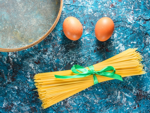 Italian pasta, sieve, eggs on a blue concrete table. Cooking process. Side view