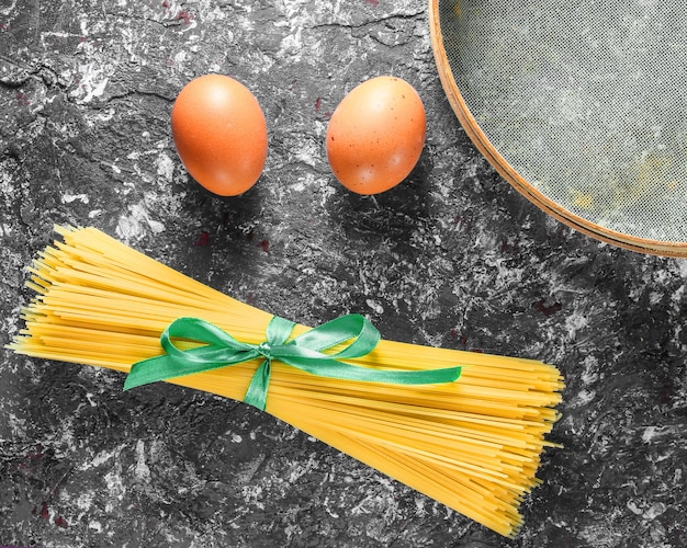 Italian pasta, sieve, eggs on gray concrete background