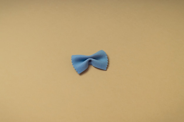 Italian pasta single blue bow tie farfalle on a yellow\
backdrop. top view. food background with copy space. flat lay with\
negative space.