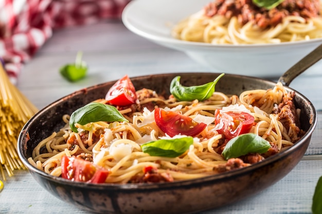 Italian pasta spaghetti bolognese in old pan with tomatoes parmesan cheese and basil.