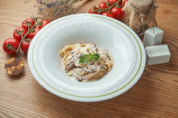 Italian pasta spaghetti with chicken and mushrooms, parmesan cheese, served in a white plate on a wooden table. Italian Cuisine