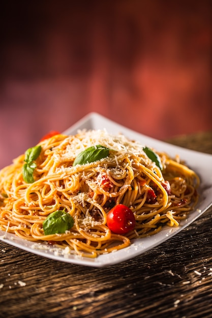 Italian pasta spaghetti with tomato sauce basil and parmesan cheese in white plate.