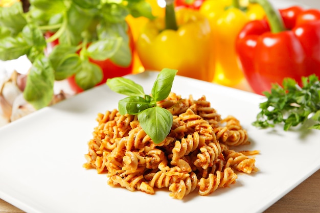 Italian pasta with red pepper pesto served on a white plate and decorated with basil