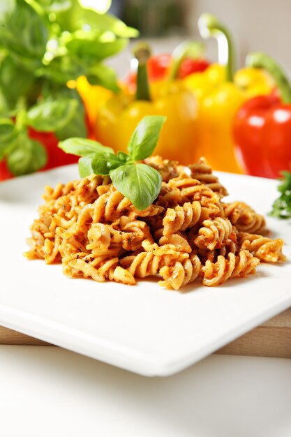 Italian pasta with red pepper pesto served on a white plate and decorated with basil