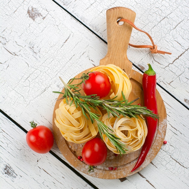 Pasta italiana con pomodori, peperoncino e rosmarino su un tavolo di legno bianco.