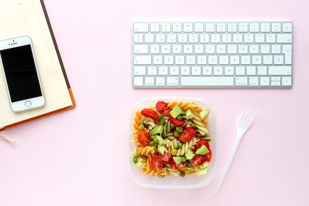 Italian pasta with vegetables on office desk with keyboard