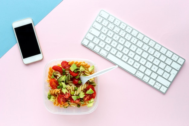 Italian pasta with vegetables on office desk with keyboard