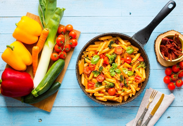 Italian penne pasta in tomato sauce and different type of vegetables, on wood