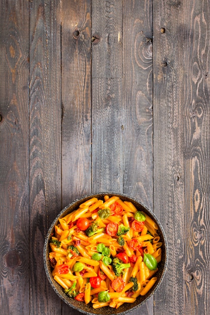 Italian penne pasta in tomato sauce and different type of vegetables, on a wooden background