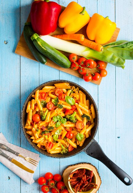 Photo italian penne pasta in tomato sauce and different type of vegetables on a wooden table