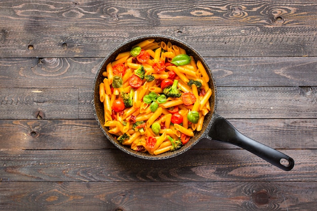 Italian penne pasta in tomato sauce and different type of vegetables, on wooden table