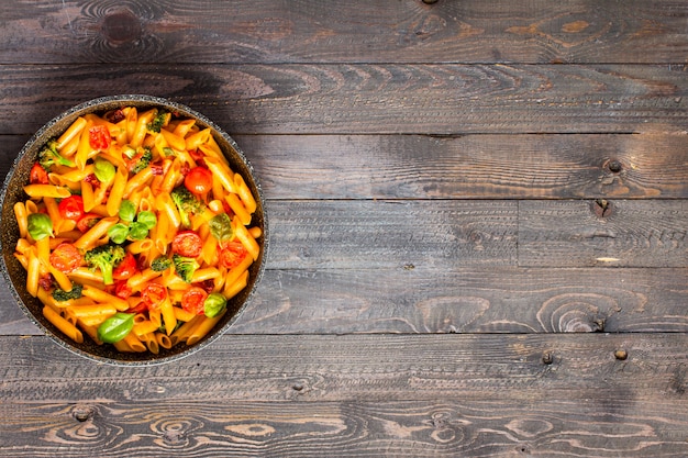 Italian penne pasta in tomato sauce and different types of vegetables, on a wooden table